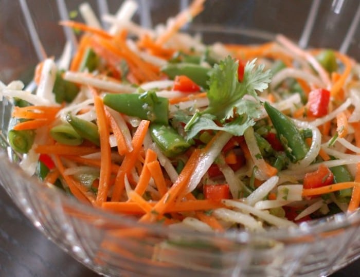 Japanese radish with bright orange carrots, red bell peppers, and snap peas tossed with a Thai citrus dressing make for a quick & easy Thai Citrus Salad Get the full vegan & nut-free recipe via JessicaLevinson.Com #VeganThaiSaladRecipe #EasyThaiSaladRecipe Close Up of Thai Citrus Salad