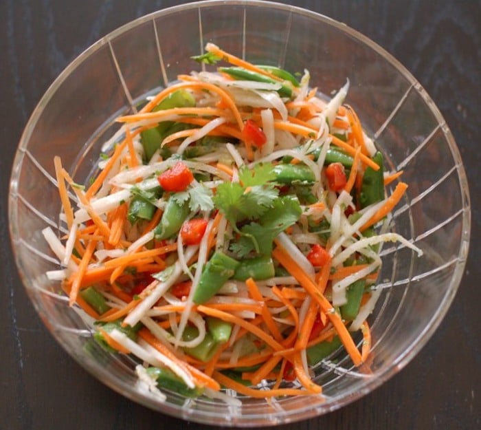 Japanese radish with bright orange carrots, red bell peppers, and snap peas tossed with a Thai citrus dressing make for a quick & easy Thai Citrus Salad Get the full vegan & nut-free recipe via JessicaLevinson.Com #VeganThaiSaladRecipe #EasyThaiSaladRecipe Thai Citrus Salad in Clear Bowl