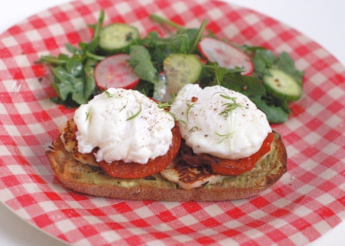 Smoky halloumi, fragrant roasted tomatoes, creamy avocado, and poached eggs top whole grain sourdough bread in this Mediterranean style egg and cheese sandwich. Get the recipe @ JessicaLevinson.com | #eggs #eggandcheese #meditteraneandiet #breakfast #brunch #breakfastfordinner #vegetarian open faced egg and cheese sandwich