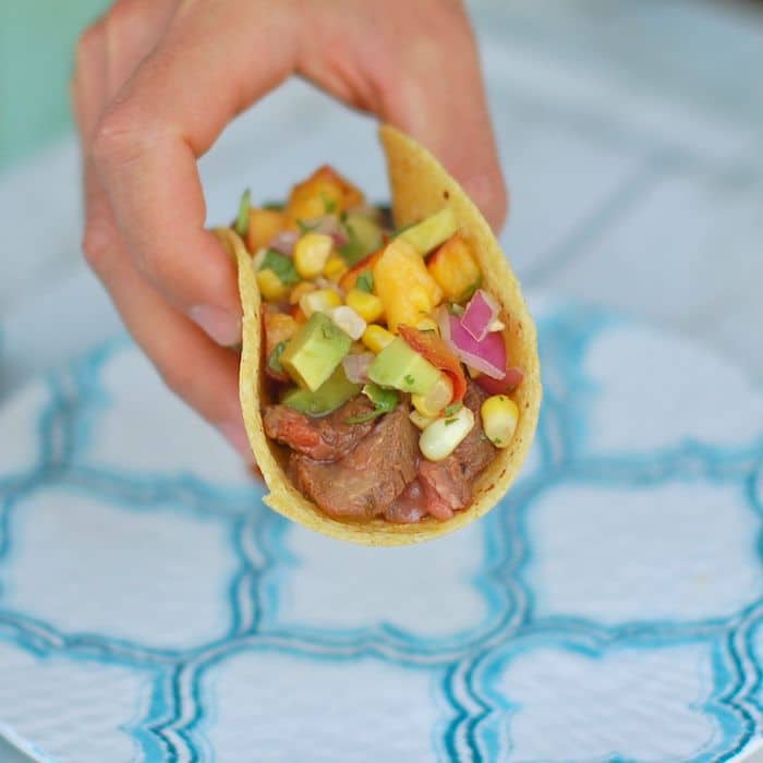 Enjoy the nutrition and health benefits of lean beef with this juicy soy-marinated flank steak taco topped with a colorful and nutritious nectarine corn salsa brimming with the flavors of summer @jlevinsonRD #sponsored #summertacos #steaktacosrecipe Hand grabbing Soy-Marinated Steak Tacos