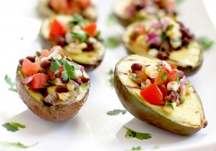 Grilled avocados are stuffed with a light and fresh mixture of corn, black beans, and tomatoes in this elegant yet simple appetizer, side dish, or entrée. Get the gluten-free and vegan recipe via JessicaLevinson.com #GrilledAvocados #StuffedAvocados Grilled Avocados with Black Bean Salsa on White Platter