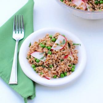 Pea and Radish Farro Salad on white plate with fork on green napkin