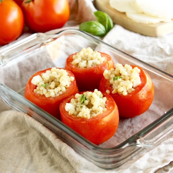 Learn about the varieties, health benefits, & culinary uses of fresh summer tomatoes. Then enjoy delicious & healthy Caprese Couscous Stuffed Tomatoes! Get the quick and easy, vegetarian recipe @jlevinsonrd #capresetomatoes #vegetarianstuffedtomatoes Caprese Couscous Stuffed Tomatoes in Glass Baking Dish