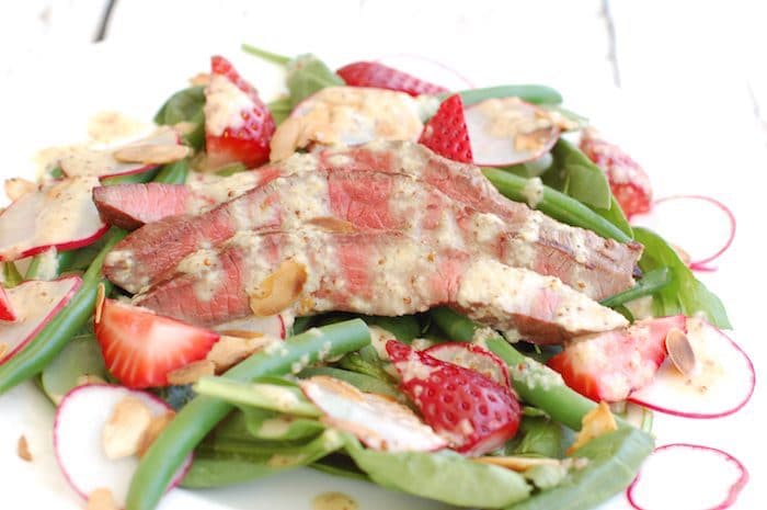 Umami-rich grilled flank steak tops a bed of baby spinach, crisp green beans, and sweet strawberries in this light summer steak salad drizzled with a sparkling, tangy Champagne shallot vinaigrette. via JessicaLevinson.com | #steaksaladrecipe #summersaladrecipe Summer Steak Salad Recipe Close Up