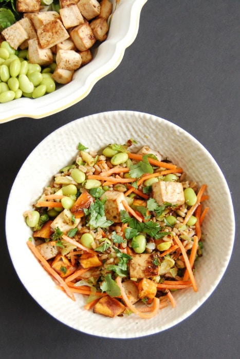 Farro Buddha Bowl with ingredients mixed in Whole grain farro is topped with shredded carrots, edamame, roasted Brussels sprouts sweet potatoes, and crispy baked tofu. Tossed with a miso lime dressing, this Asian-Style Farro Buddha Bowl is a vegetarian and vegan-friendly meal the whole family will love.