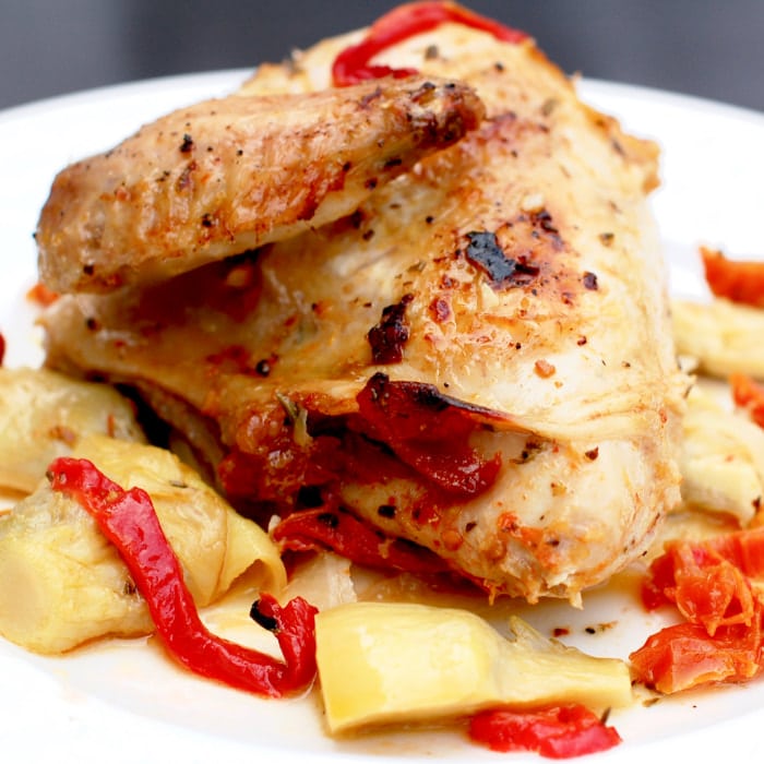 Roasted chicken with artichokes, peppers, and sun-dried tomatoes can be made in under an hour and is a complete meal. plate of roasted chicken with artichokes