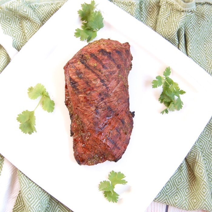 Perfectly grilled Cilantro Lime Steak is easy to make and a delicious entrée to serve guests at your summer barbecue. Recipe via JessicaLevinson.com | #GrilledSteakRecipe #SteakMarinadeRecipe Grilled Cilantro Lime Steak on White Plate