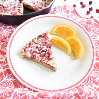 slice of cranberry orange dutch baby on plate with orange slices